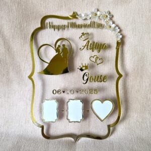 Close-up of a personalized gold acrylic wedding thumb board displaying the names 'Asfiya' and 'Gouse', the date '06-10-2025', a couple's silhouette, and thumbprint areas, on a light beige textured surface.