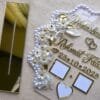 Close-up angle of the personalized Nikah thumb board, showing the 3D texture of the gold acrylic names and the intricate details of the floral and pearl embellishments.