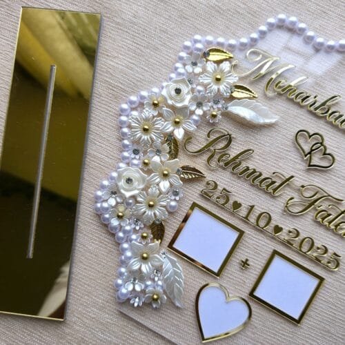 Close-up angle of the personalized Nikah thumb board, showing the 3D texture of the gold acrylic names and the intricate details of the floral and pearl embellishments.