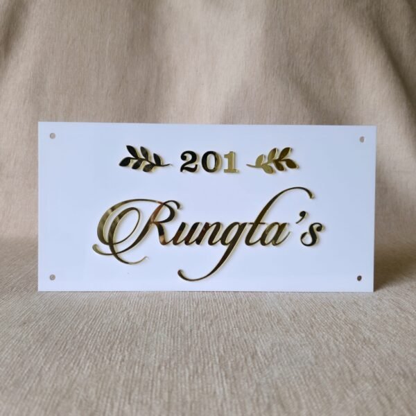 A front-on view of a white acrylic name plate featuring elegant 3D golden "201 Rungta's" lettering and golden leaf accents, resting on a beige fabric surface.