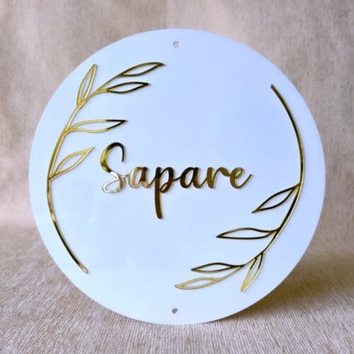 Front-on view of the custom round acrylic name plate in white and gold, showing the pre-drilled holes for mounting.