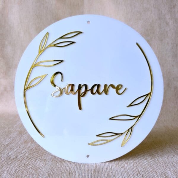 Front-on view of the custom round acrylic name plate in white and gold, showing the pre-drilled holes for mounting.